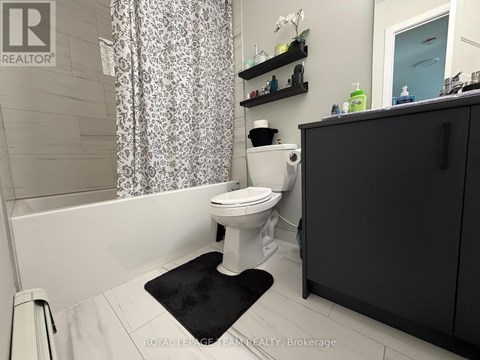 A white toilet in a bathroom with a black mat in front of it.