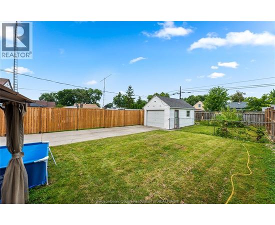 A backyard with a white house, a blue tarp, and a wooden fence.