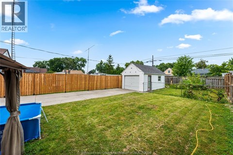 A backyard with a white house, a blue tarp, and a wooden fence.