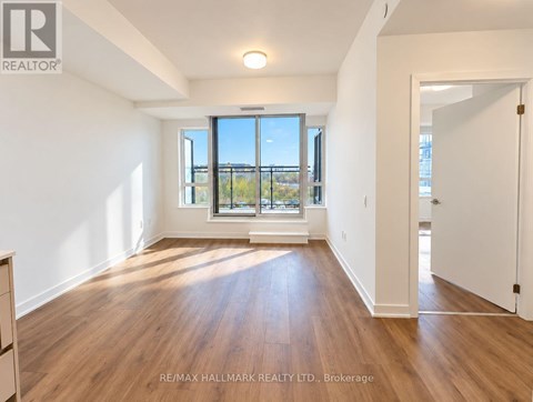 A spacious room with wooden flooring and a large window overlooking a balcony.