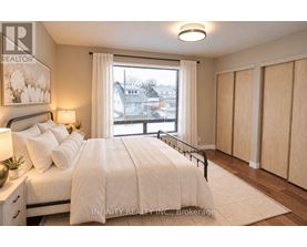 A bedroom with a large bed, a nightstand with a lamp, and a window with a view of the neighborhood.