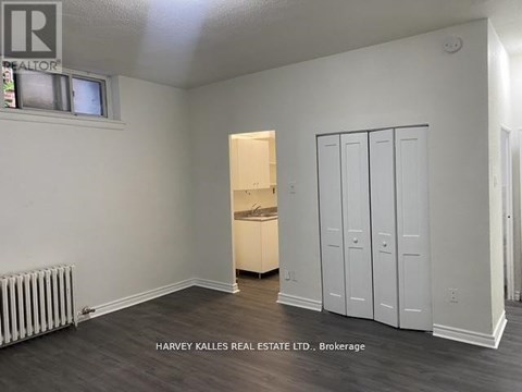 A room with a white wall and a wooden floor with a white cabinet and a window.