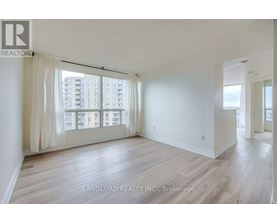 A spacious room with wooden flooring and large windows overlooking a cityscape.