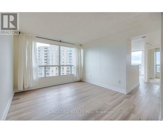 A spacious room with wooden flooring and large windows overlooking a cityscape.