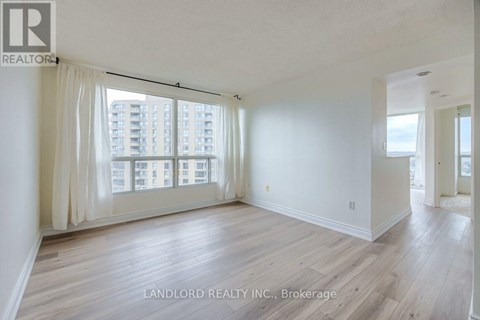 A spacious room with wooden flooring and large windows overlooking a cityscape.