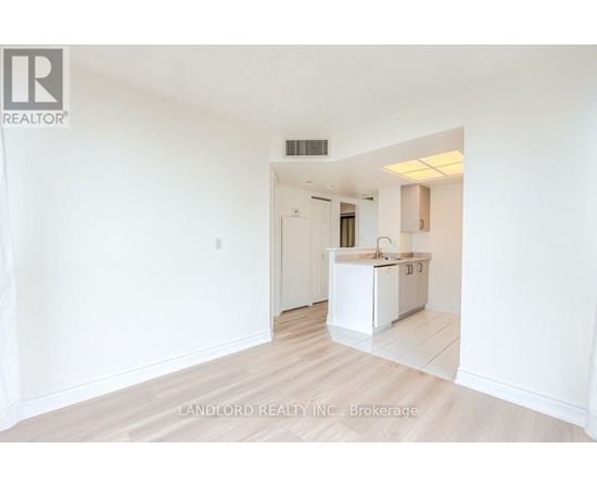 A white kitchen with a sink and cabinets is seen in a room with white walls and wooden flooring.