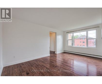 A room with wooden flooring and white walls, with a window showing a red building outside.