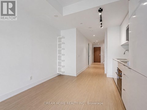 A white interior space with a wooden floor and a staircase on the left.