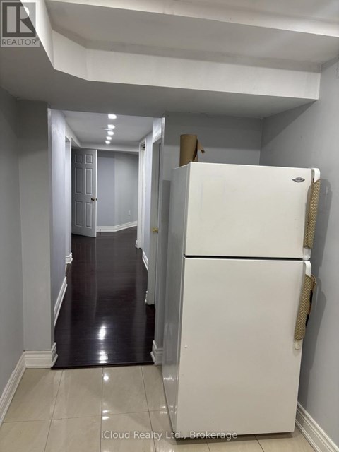 A white refrigerator stands in a narrow hallway with a door at the end.