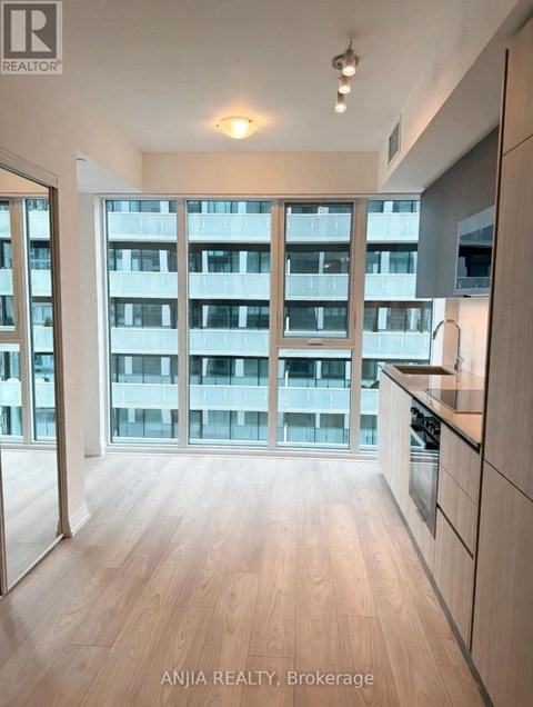 A well-lit kitchen with wooden floors and a large window overlooking a building.