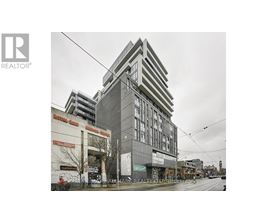 A tall building with a grey facade stands in the middle of a street.