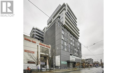 A tall building with a grey facade stands in the middle of a street.