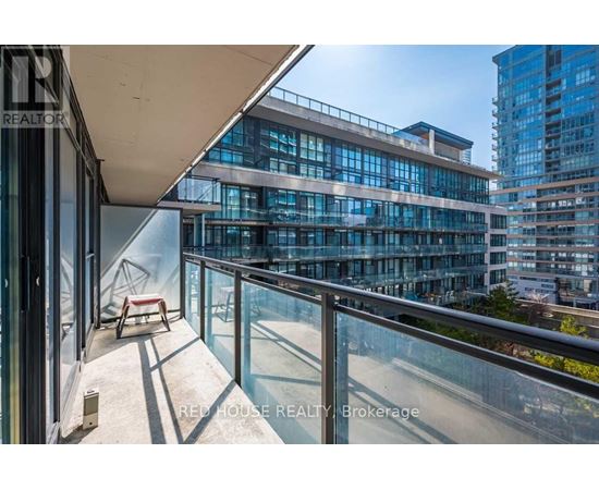 A balcony with a glass railing and a red chair overlooks a cityscape.
