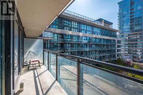 A balcony with a glass railing and a red chair overlooks a cityscape.