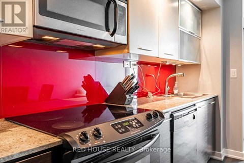 A modern kitchen with a red backsplash and stainless steel appliances.