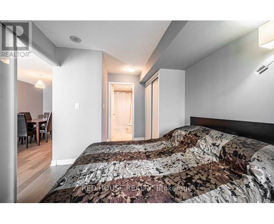 A bedroom with a large bed and a dining area in the background.