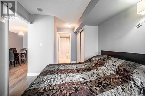 A bedroom with a large bed and a dining area in the background.