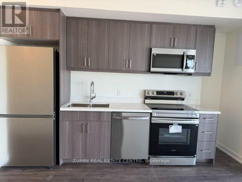 A kitchen with a refrigerator, microwave, oven, and sink.