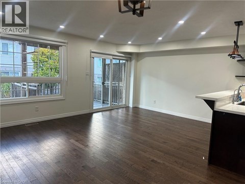 A room with wooden flooring and a large window with a view of trees and a fence.