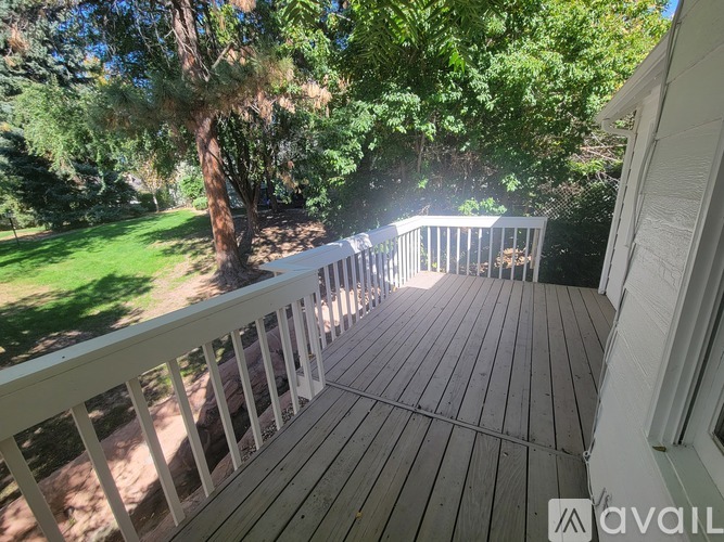 A wooden deck with a white railing and trees in the background.