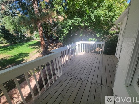 A wooden deck with a white railing and trees in the background.