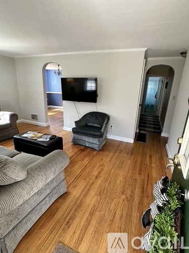 A living room with a grey couch, a black ottoman, and a television mounted on the wall.