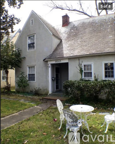 A white house with a grey roof and a white table and chairs in front of it.