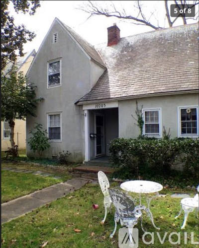 A white house with a grey roof and a white table and chairs in front of it.