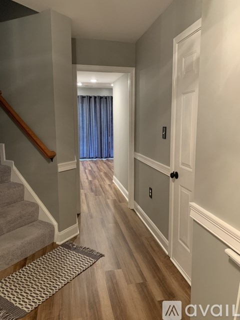 A hallway with a wooden floor, a staircase with a wooden handrail, and a door with a black handle.