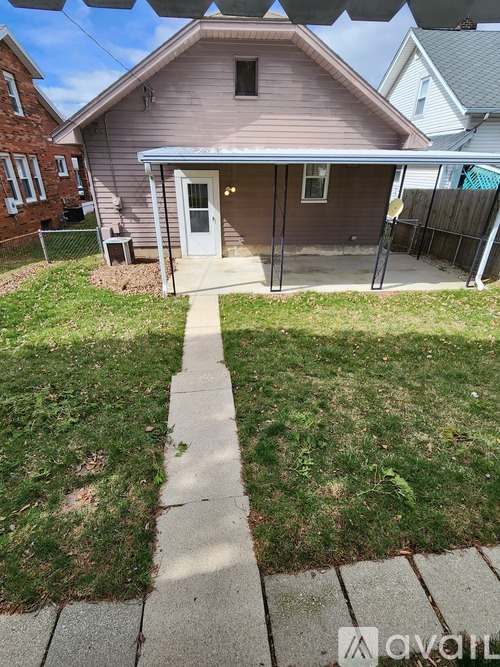 A house with a brown roof and a white door is surrounded by a grassy area and a sidewalk.