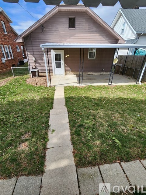 A house with a brown roof and a white door is surrounded by a grassy area and a sidewalk.