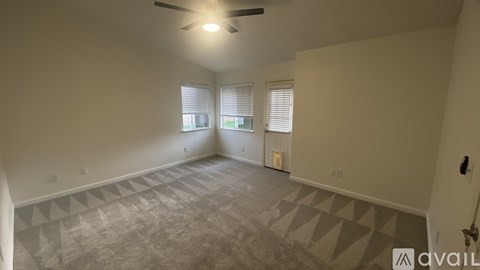 A spacious room with a ceiling fan and patterned carpeting.