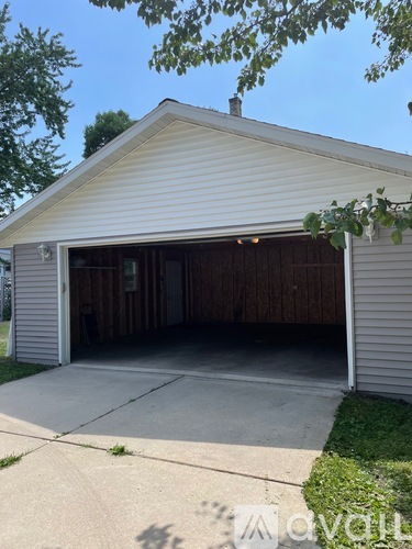 A detached garage with a white siding and a brown wooden door.