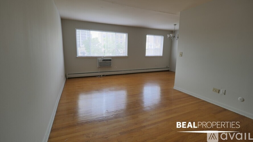 A spacious room with wooden flooring and two windows.