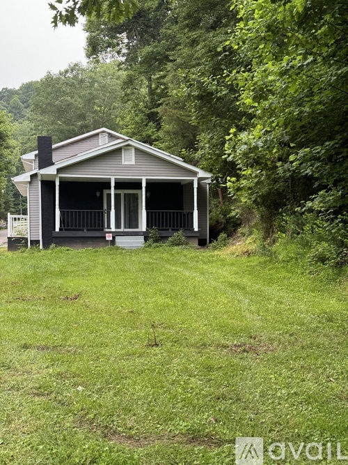 A small house with a porch is surrounded by greenery.