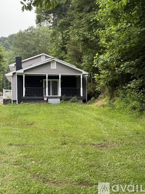 A small house with a porch is surrounded by greenery.