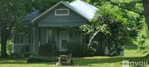 A blue house with a porch and a tree in front.