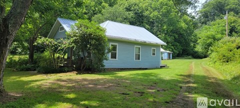 A blue house with a white roof is surrounded by greenery.