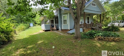 A small blue house with a porch and a tree in front.