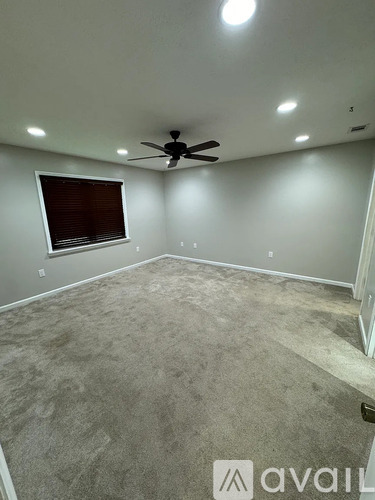 A room with a carpeted floor, a ceiling fan, and a window with blinds.