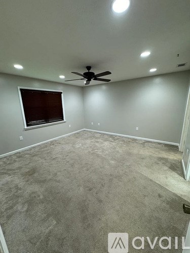 A room with a carpeted floor, a ceiling fan, and a window with blinds.