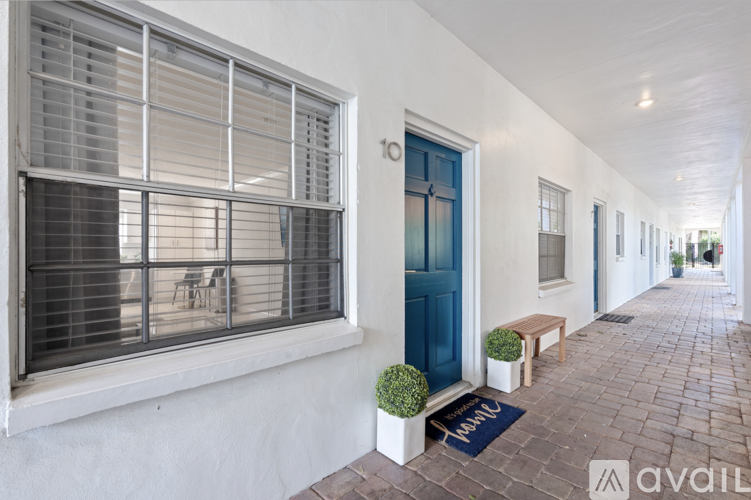A long white building with a blue door and a mat on the ground.