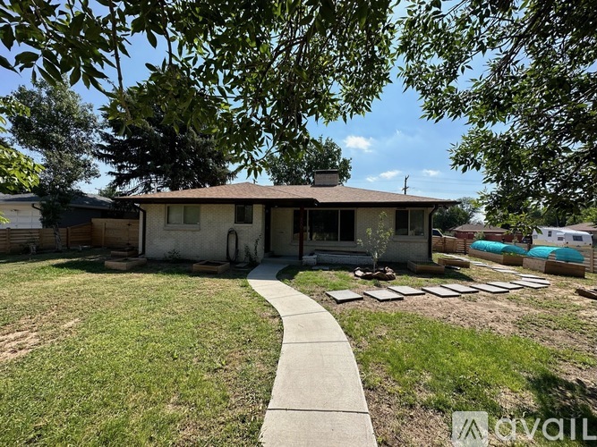 A house with a brown roof and a white fence is surrounded by a grassy area and trees.