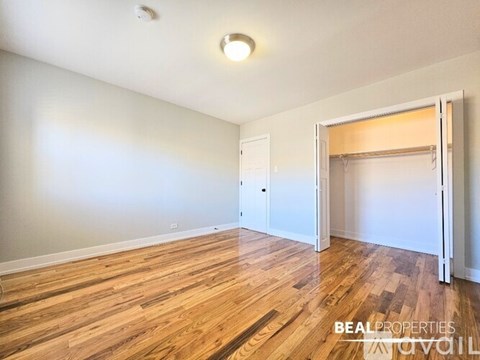 A room with wooden flooring and white walls, with a door and a window.