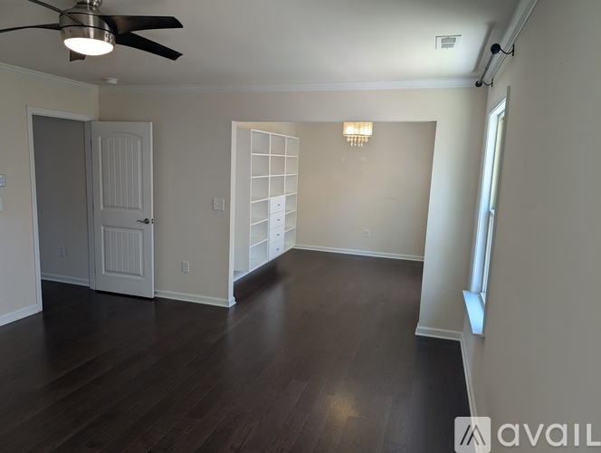 A spacious room with a ceiling fan and dark wood flooring.