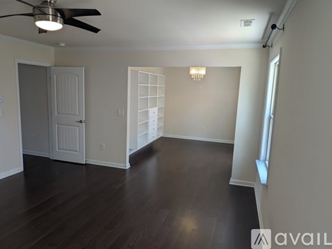 A spacious room with a ceiling fan and dark wood flooring.