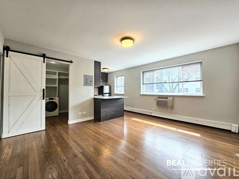 A spacious room with wooden flooring and a sliding door leading to a laundry area.