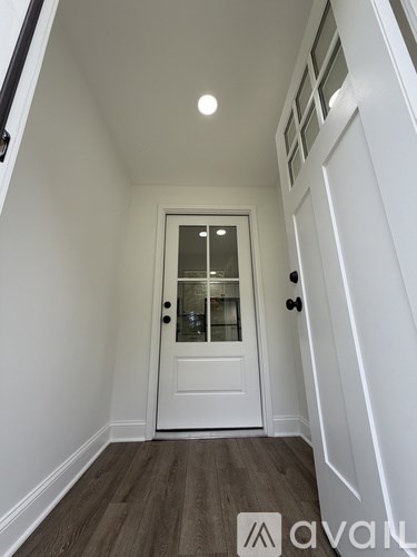 A white door with a glass window is in the middle of a hallway with a wooden floor.