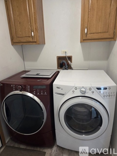 Two washing machines, one maroon and one white, are in a laundry room with wooden cabinets.