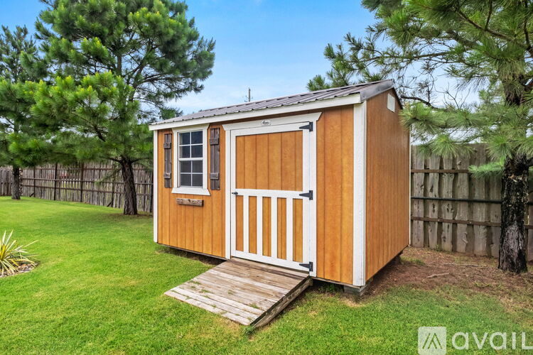 A wooden shed with a brown door and windows is situated in a grassy area.